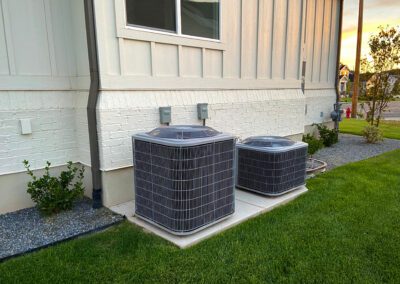 Two central air conditioning units outside of a residential building at dusk.
